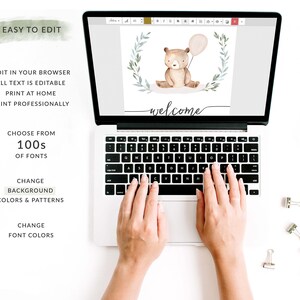 May include: A laptop computer with a white background showing a digital design of a brown bear holding a balloon with a green leafy wreath around it. The text "welcome" is written in cursive below the bear. The laptop keyboard is visible with hands typing on it.