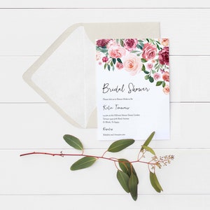 Op de afbeelding: Een witte bruiloftsdouche-uitnodiging met een bloemenontwerp in roze en bordeauxrode tinten. De tekst luidt "Bridal Shower" en "Wordt u alstublieft uitgenodigd om de bruid Katie Timmons te verwennen".