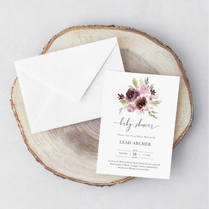 May include: A white card with a floral design in shades of pink and purple. The text on the card reads "baby shower" and "Please Join Us to Honor Mom-to-Be Leah Archer" with the date and time of the event.