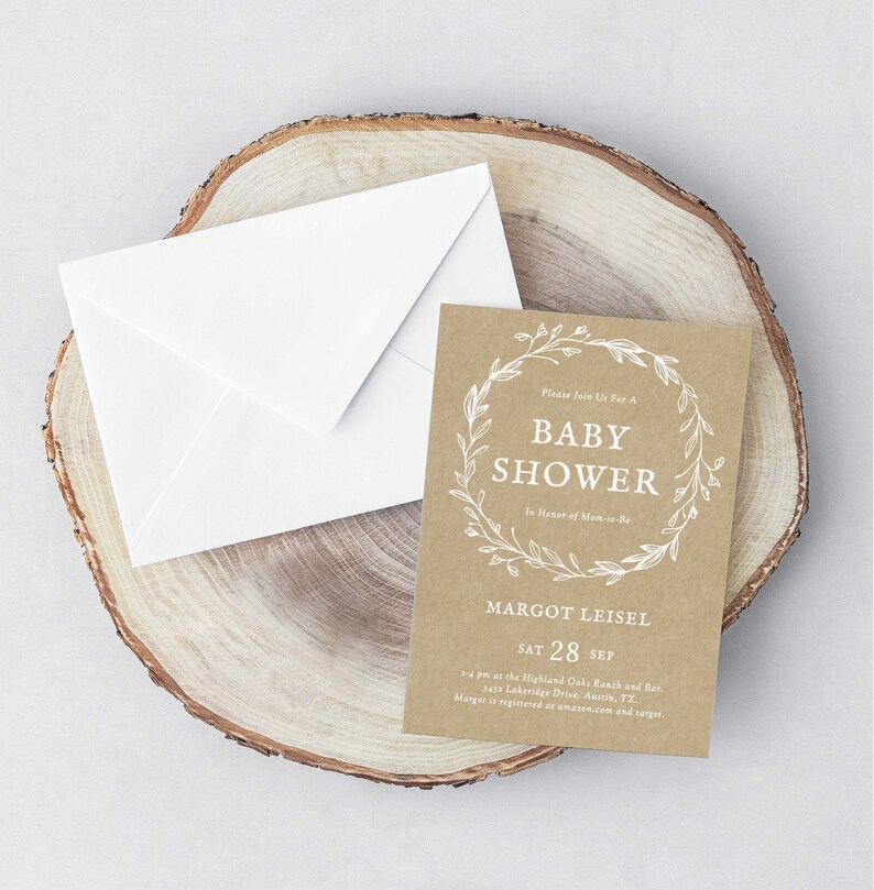 May include: A kraft paper baby shower invitation with white text and a floral wreath design. The invitation reads "Please join us for a Baby Shower in honor of Mom-to-be Margot Leisel, Sat 28 Sep, 2-4 pm at the Highland Oaks Ranch and Bar, 3435 Lakeridge Drive, Austin, TX. Margot is registered at amazon.com and target."
