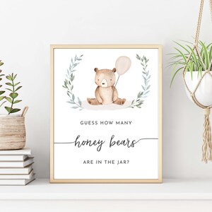 May include: A printable baby shower game sign with a watercolor illustration of a brown bear holding a pink balloon. The sign says "Guess how many honey bears are in the jar?"