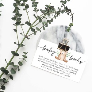 May include: A white card with the text "baby books" and a small illustration of a brown bear with green leaves. The text reads: "One small request that isn't too hard. Please bring a book instead of a card. By signing your book we'll remember and share, your special gift, even when you're not there."