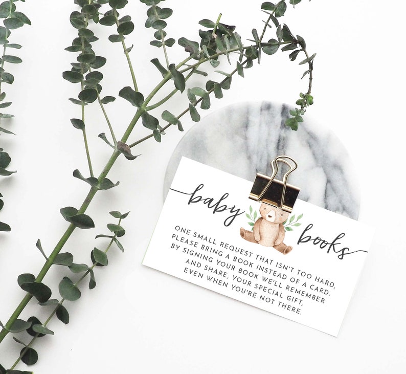 May include: A white card with the text "baby books" and a small illustration of a brown bear with green leaves. The text reads: "One small request that isn't too hard. Please bring a book instead of a card. By signing your book we'll remember and share, your special gift, even when you're not there."
