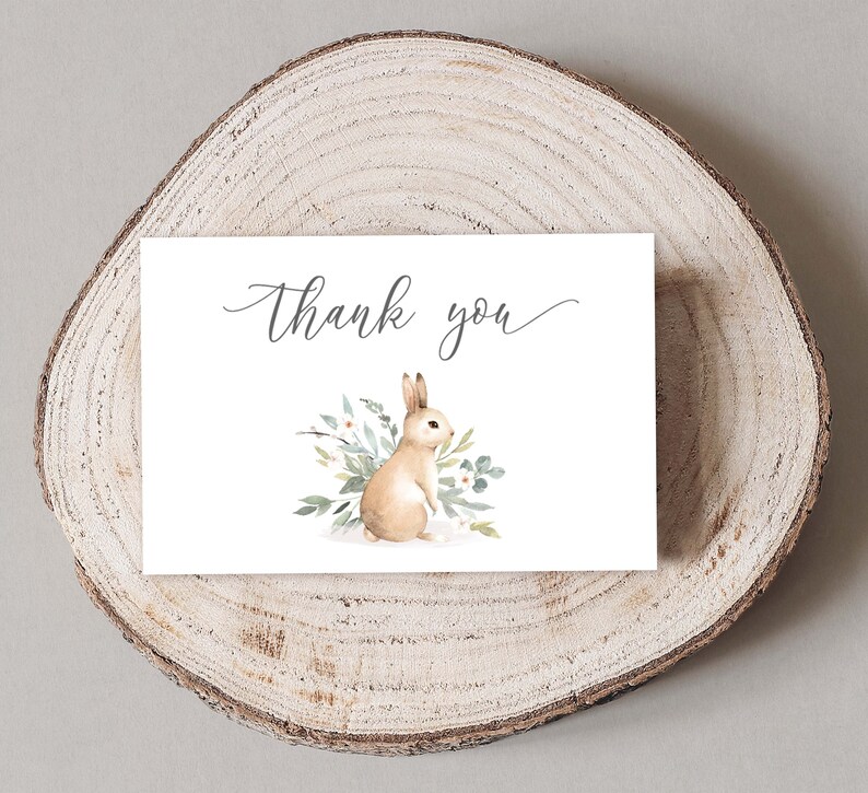 May include: A white thank you card with a watercolor illustration of a brown rabbit with a white tail sitting in a bed of green leaves and white flowers. The text "Thank you" is written in cursive on the card.