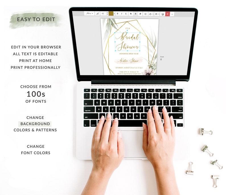 May include: A laptop computer with a screen displaying a customizable bridal shower invitation template. The invitation features a gold geometric frame with green foliage and the text "It's a Bridal Shower" in a gold script font. The text "Honoring Bride-to-Be" is in a smaller font below the main text. The invitation also includes the bride's name, the date, time, and location of the shower. The laptop is on a white surface with paper clips.