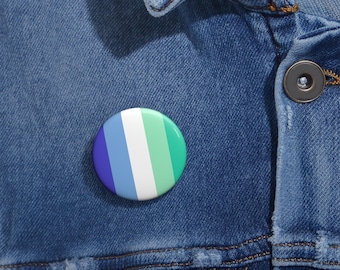 Puede incluir: Un pin de botón a rayas azul, blanco y verde. El pin está en una chaqueta vaquera.