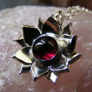 May include: A silver pendant in the shape of a flower with a red gemstone in the center.