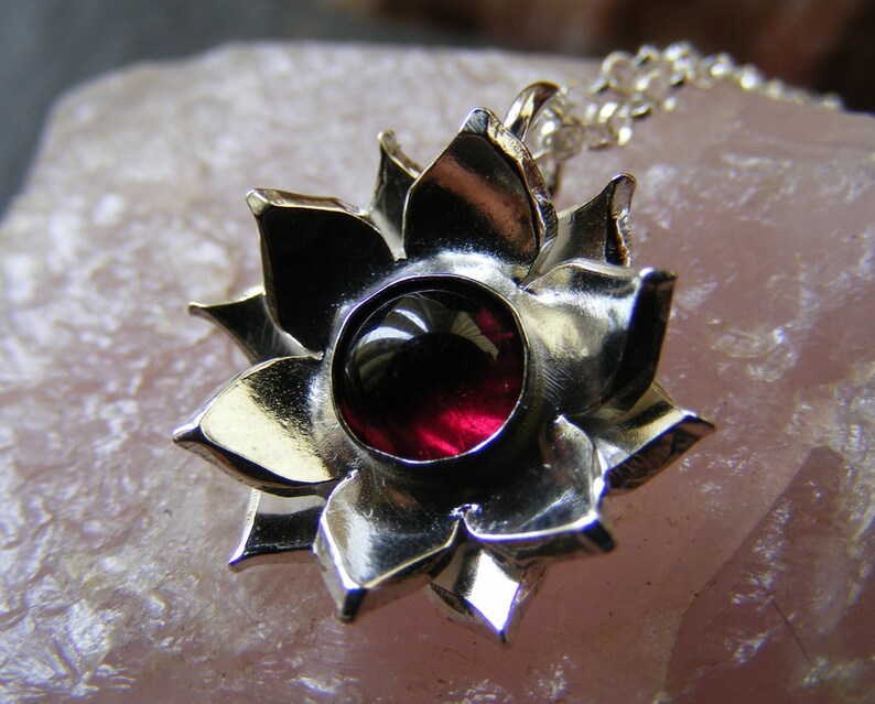 May include: A silver pendant in the shape of a flower with a red gemstone in the center.