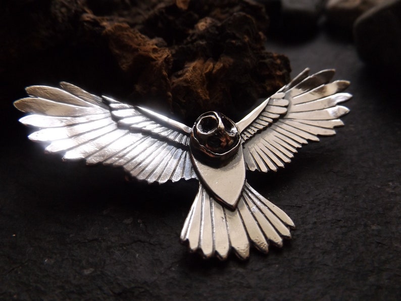 May include: A silver owl pendant with detailed wings and a textured body. The owl is in flight with its wings spread wide.