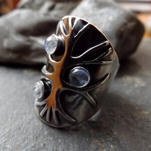 May include: A silver ring with a tree design and three moonstone gems.