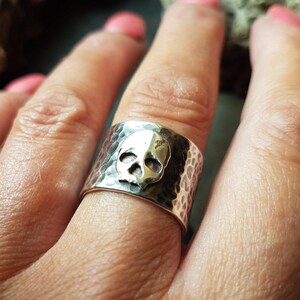 May include: A silver ring with a hammered finish and a skull design. The skull is raised and has a slightly oxidised finish.
