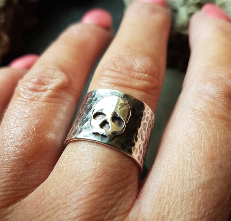 May include: A silver ring with a hammered finish and a skull design. The skull is raised and has a slightly oxidised finish.