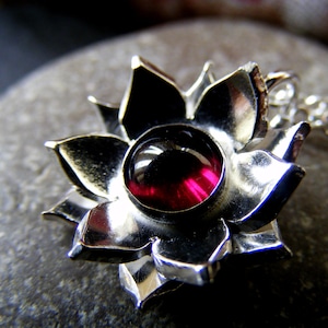 May include: A silver pendant in the shape of a flower with a dark red gemstone in the center.