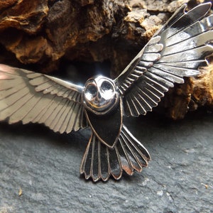 May include: A silver owl pendant with detailed wings and a black body. The owl is in flight with its wings spread wide.