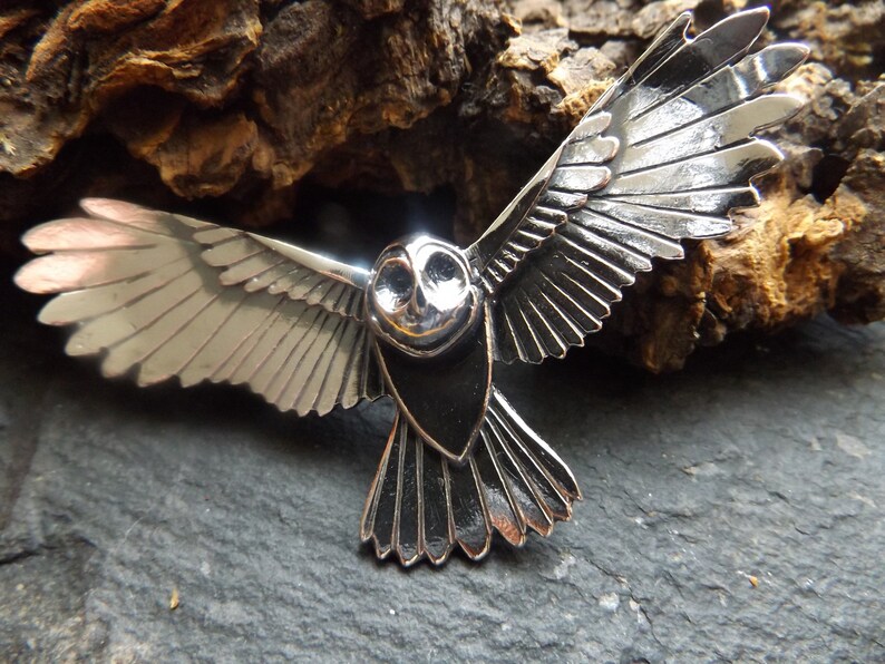 May include: A silver owl pendant with detailed wings and a black body. The owl is in flight with its wings spread wide.