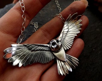 May include: A silver owl pendant necklace with detailed wings and a realistic owl face. The pendant is attached to a silver chain.