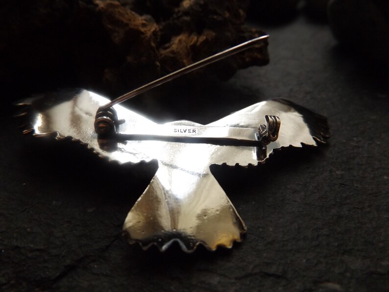 May include: Silver eagle brooch with a detailed design and a pin closure. The back of the brooch is marked "SILVER".