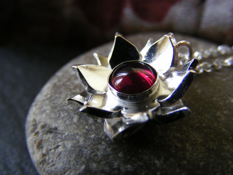 May include: A silver pendant in the shape of a flower with a red gemstone in the center.