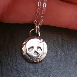 May include: A silver necklace with a small, round pendant featuring a textured skull design.