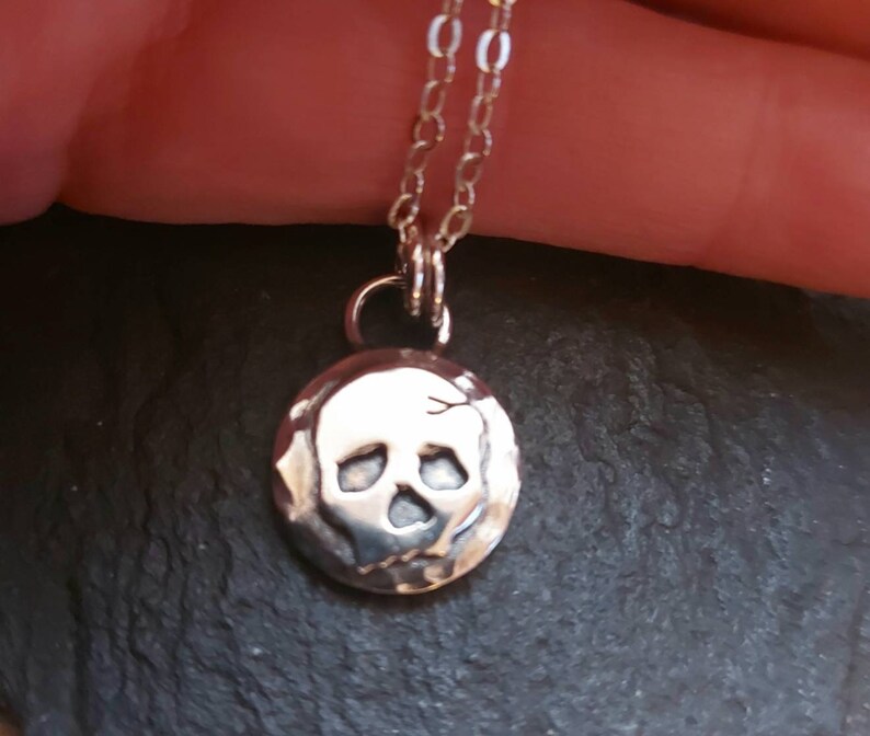 May include: A silver necklace with a small, round pendant featuring a textured skull design.