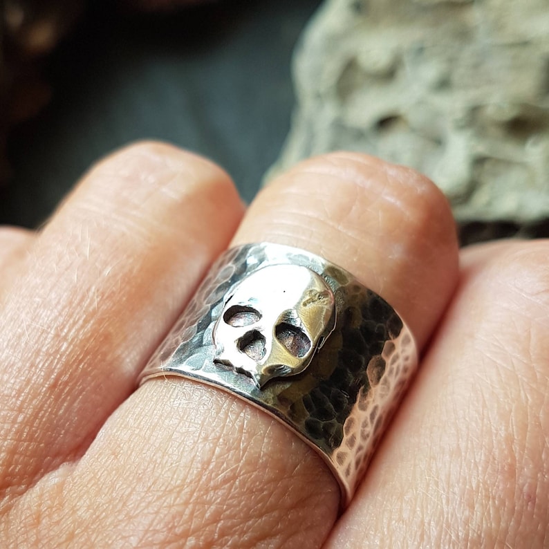 May include: A silver skull ring with a hammered finish. The skull is raised and has a textured surface.