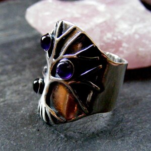 May include: A silver ring with a tree design and three amethyst stones. The ring is set on a gray background.