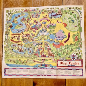 May include: Vintage Magic Kingdom map featuring colorful illustrations of park attractions, including Fantasyland and Tomorrowland. The map includes a list of attractions and a compass rose. The map is on a slightly aged paper.