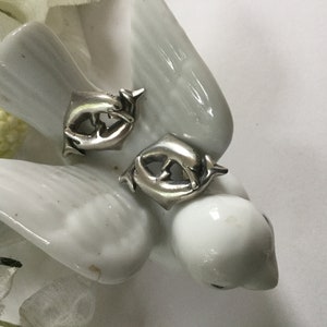 May include: A pair of silver earrings featuring a dolphin design. The dolphins are facing each other and appear to be swimming.