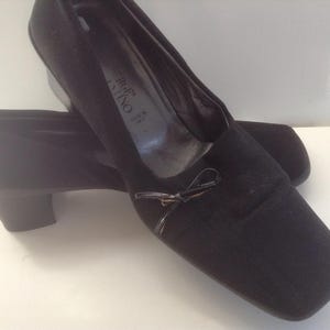 May include: Black suede heeled shoes with a bow detail. The shoes are made in Italy and have a square toe.