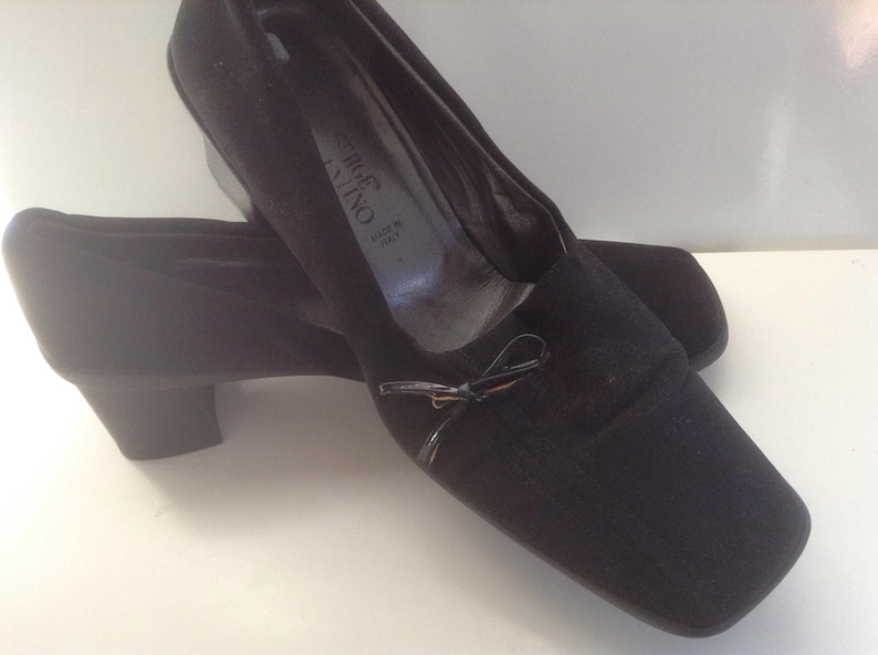 May include: Black suede heeled shoes with a bow detail. The shoes are made in Italy and have a square toe.