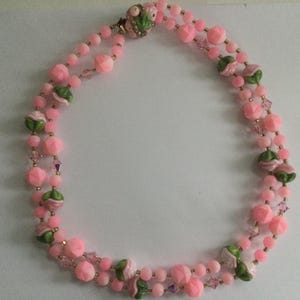 May include: A pink and green beaded necklace with flower accents. The necklace is made of glass beads and has a gold clasp.