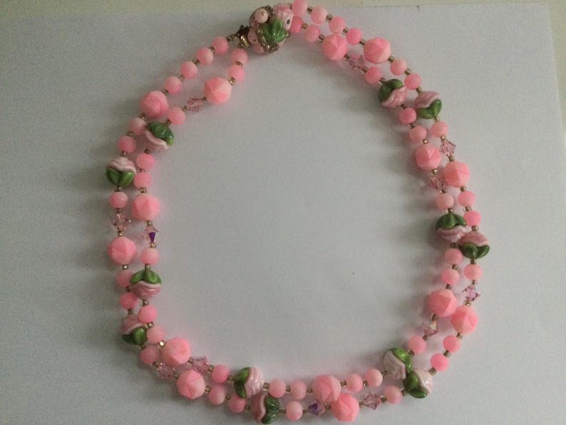 May include: A pink and green beaded necklace with flower accents. The necklace is made of glass beads and has a gold clasp.