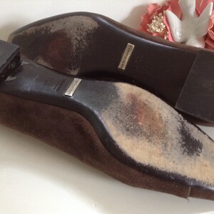 May include: A pair of brown suede flats with leather soles. The soles are worn and show signs of use. The shoes have a silver label that reads "MADE IN ITALY" and "GIUSEPPE ZANOTTI".