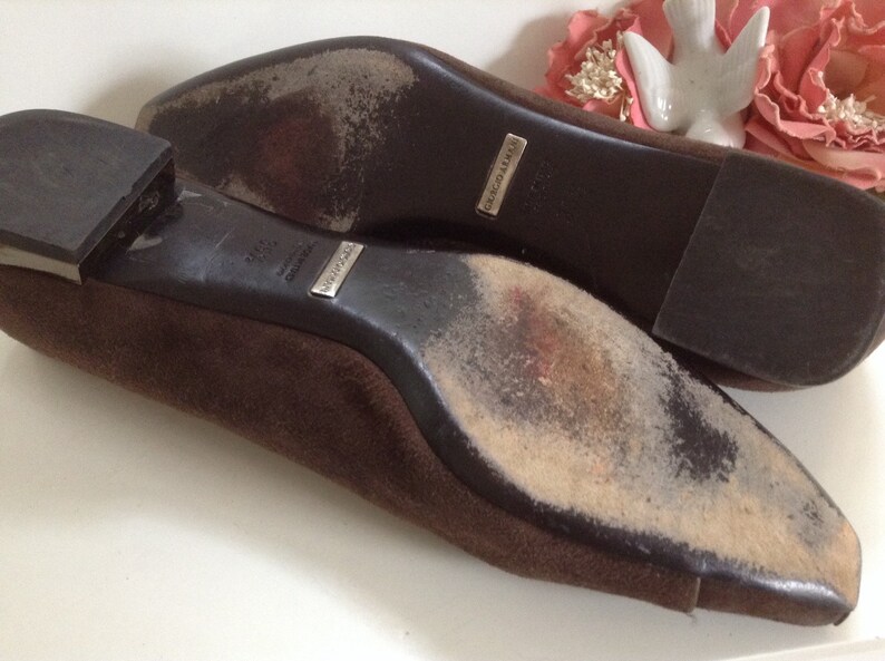 May include: A pair of brown suede flats with leather soles. The soles are worn and show signs of use. The shoes have a silver label that reads "MADE IN ITALY" and "GIUSEPPE ZANOTTI".