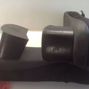 May include: A pair of black heeled shoes with a thick rubber sole. The shoes are broken in half, showing the inside of the shoe.