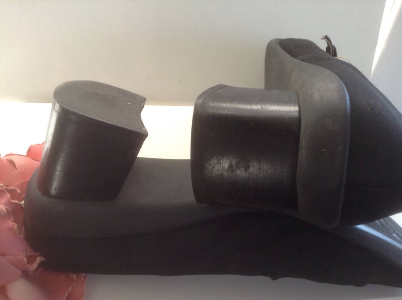 May include: A pair of black heeled shoes with a thick rubber sole. The shoes are broken in half, showing the inside of the shoe.