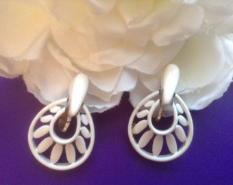 May include: A pair of white clip-on earrings with a circular design featuring a smaller circle inside. The earrings have a delicate, intricate pattern.