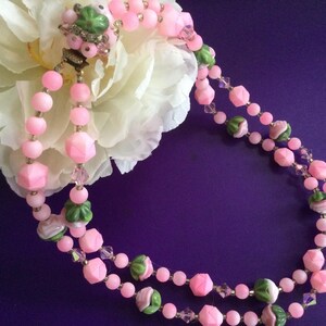 May include: A double strand pink and green glass bead necklace with flower accents. The necklace is on a purple background.
