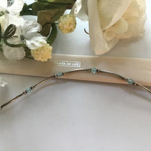 May include: A silver bracelet with light blue beads and the text "PLATA DE LEY" on a white background.