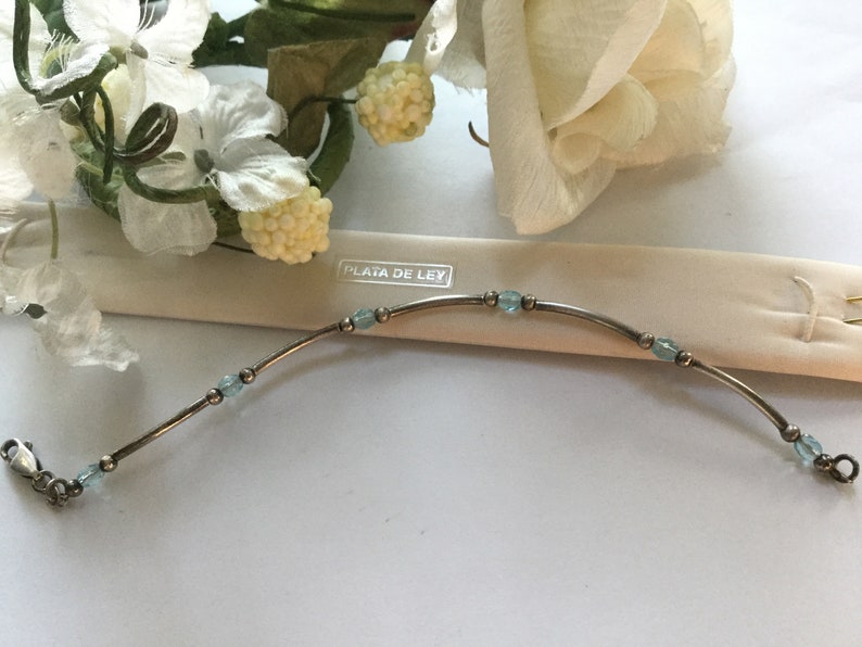 May include: A silver bracelet with light blue beads and the text "PLATA DE LEY" on a white background.