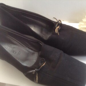 May include: A pair of black suede shoes with a bow detail and the brand name "Salvatore Ferragamo" printed on the insole.