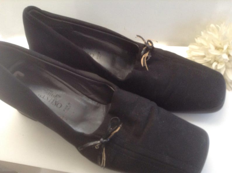 May include: A pair of black suede shoes with a bow detail and the brand name "Salvatore Ferragamo" printed on the insole.
