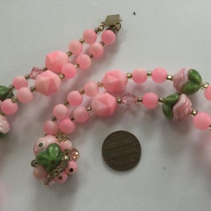 May include: A pink and green glass bead necklace with rose-shaped beads and a gold clasp.
