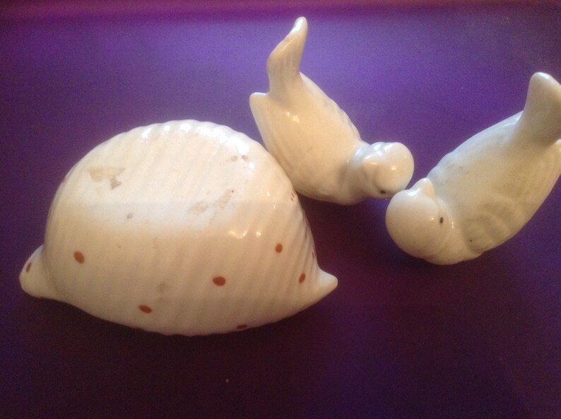Puede incluir: Una concha de cer&aacute;mica blanca con lunares marrones y dos p&aacute;jaros de cer&aacute;mica blanca. Los p&aacute;jaros se miran, con el pico de uno tocando la cabeza del otro.