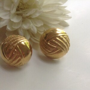 May include: A pair of gold-tone earrings with a woven design. The earrings are round and have a smooth, polished finish.