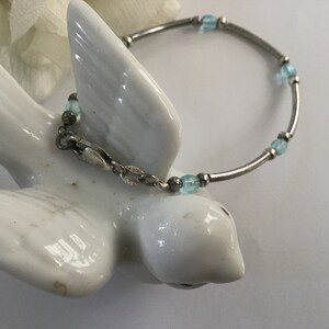 May include: A silver bracelet with light blue glass beads. The bracelet has a clasp closure.