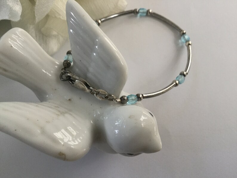 May include: A silver bracelet with light blue glass beads. The bracelet has a clasp closure.