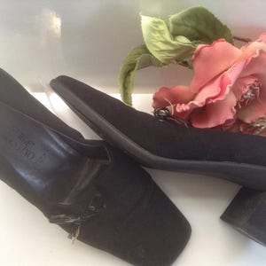 May include: A pair of black heeled shoes with a small bow detail on the front. The shoes are made of a soft fabric and have a block heel.