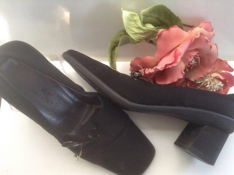May include: A pair of black heeled shoes with a small bow detail on the front. The shoes are made of a soft fabric and have a block heel.