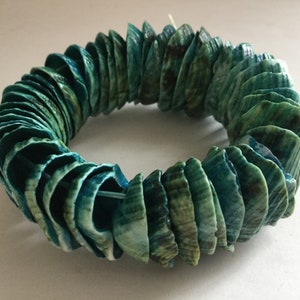 Könnte beinhalten: Ein türkisfarbenes und grünes Muschel-Armband aus vielen kleinen Muscheln. Die Muscheln sind kreisförmig angeordnet und durch einen dünnen Draht zusammengehalten.